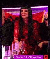 a woman in a red dress is sitting at a table with wine glasses and a sign that says albania