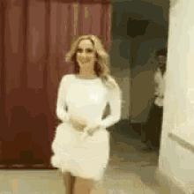 a woman in a white dress is standing in a room with a red curtain .