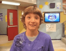 a young boy wearing a purple shirt is smiling in front of a tv screen that says ' hot wheels ' on it