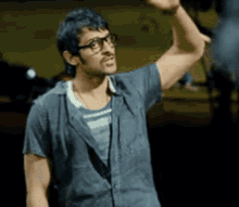 a man wearing glasses and a blue shirt is raising his hand in the air