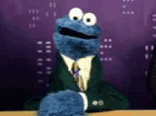a cookie monster in a suit and tie sitting at a table