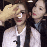 a woman is applying makeup to another woman 's face with a sticker that says ( ) on it
