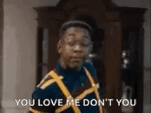 a man in a blue shirt and yellow vest is standing in front of a cabinet and says `` you love me don t you ''