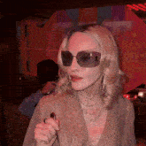 a woman wearing sunglasses and a necklace with a cross has a ring on her finger