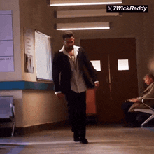 a man in a suit is walking down a hallway with a sign that says x7wick reddy on it