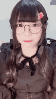 a girl wearing glasses and a black dress has a flower in her hair .