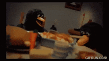 a gif from gifrun.com shows a penguin sitting at a table with food