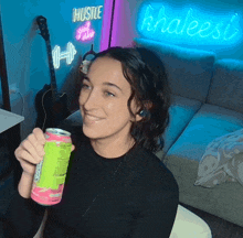 a woman holds a can of soda in front of a sign that says hustle
