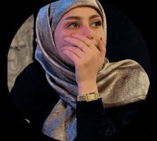 a woman wearing a hijab and a watch covers her mouth