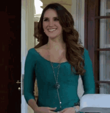 a woman in a green top and necklace smiles