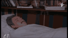 a man with a mustache is laying in a bed with the letters lt on the bottom left