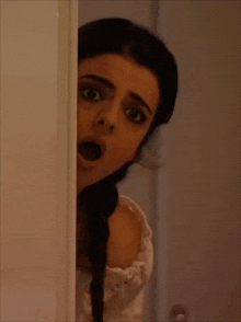 a woman covering her mouth with her hand while peeking out of a doorway