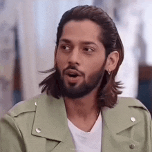 a man with long hair and a beard is wearing a green leather jacket and earrings .