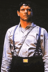 a man wearing suspenders and a white shirt has a yellow badge on his belt