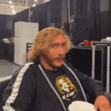 a man with blonde curly hair is wearing a black shirt with a picture of a skull on it