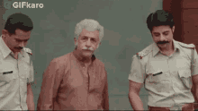 a man with a mustache is being escorted by two police officers in front of a building .