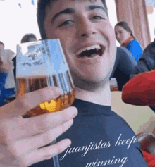 a man holding a glass of beer with juanjistas keep winning on his shirt