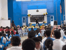 a large group of people are sitting in front of a stage with a sign that says " selamat hari guru "