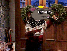 a cartoon mouse with a crown on its head is holding a wreath in front of a door