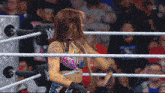 a woman is standing in a wrestling ring with a w logo on the ropes