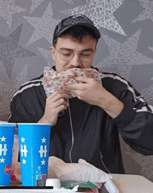 a man sitting at a table eating a sandwich next to a cup that says h on it