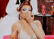 a woman covering her mouth with her hand while drinking from a pink can with a straw