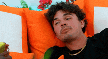 a man with curly hair is laying on a couch with orange pillows .