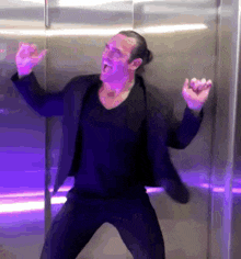 a man in a black jacket is dancing in an elevator with his arms outstretched