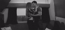 a black and white photo of a man and a woman kissing on a train .