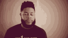 a man with a beard is standing with his eyes closed and wearing a black shirt .