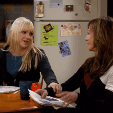 two women are sitting at a table in front of a refrigerator with a sticker on it that says ' beef ' on it