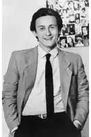 a young man wearing a suit and tie is standing in front of a wall with pictures of people on it .