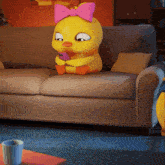 a yellow stuffed duck with a pink bow on its head sits on a couch