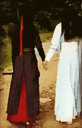 a man and a woman holding hands while walking down a path
