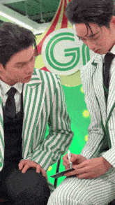 two men in green and white striped suits are looking at a piece of paper