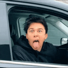 a man in a black hoodie is sticking his tongue out while sitting in a car .