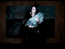 a woman in a black jacket is holding a plastic bag in front of a painting