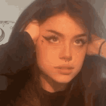 a girl with a cross tattoo on her face is holding her head .