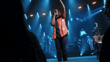a man in an orange shirt is singing into a microphone on stage