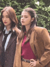 two women wearing suits and ties are standing next to each other in front of a bush .