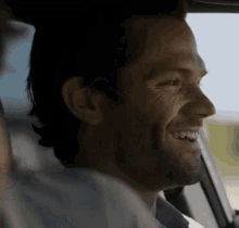 a man with a beard is smiling while sitting in a car .