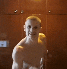 a man without a shirt is standing in front of a wooden cabinet