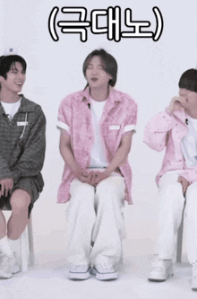 a man in a pink shirt is sitting next to two other men in white pants