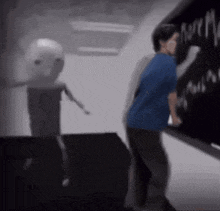 a man in a blue shirt is writing on a blackboard while a robot stands behind him