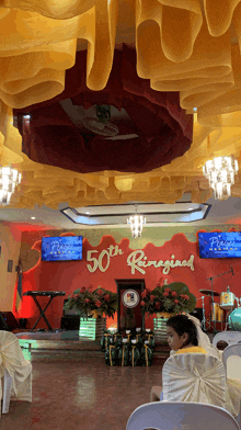 a girl sits at a table in front of a wall that says 50th ringigial