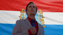 a man in a suit stands in front of a flag