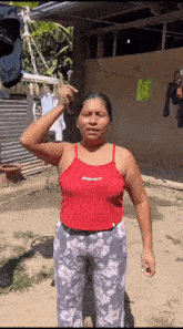 a woman in a red tank top and floral pants is giving a thumbs up .