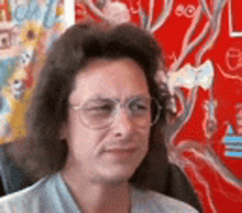 a woman with long hair and glasses is sitting in front of a red wall .