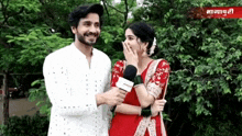 a man and a woman are standing next to each other and the woman is covering her mouth with her hand .
