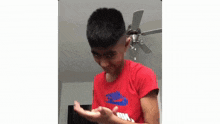 a young boy wearing a red nike shirt is standing in front of a ceiling fan in a living room .